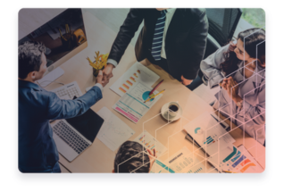 A group of business individuals shaking and with charts on the table.